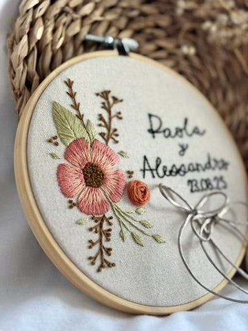 Porta alianzas en bastidor bordado a mano sobre algodón natural, con nombres bordados y motivos florales boho para boda personalizada.