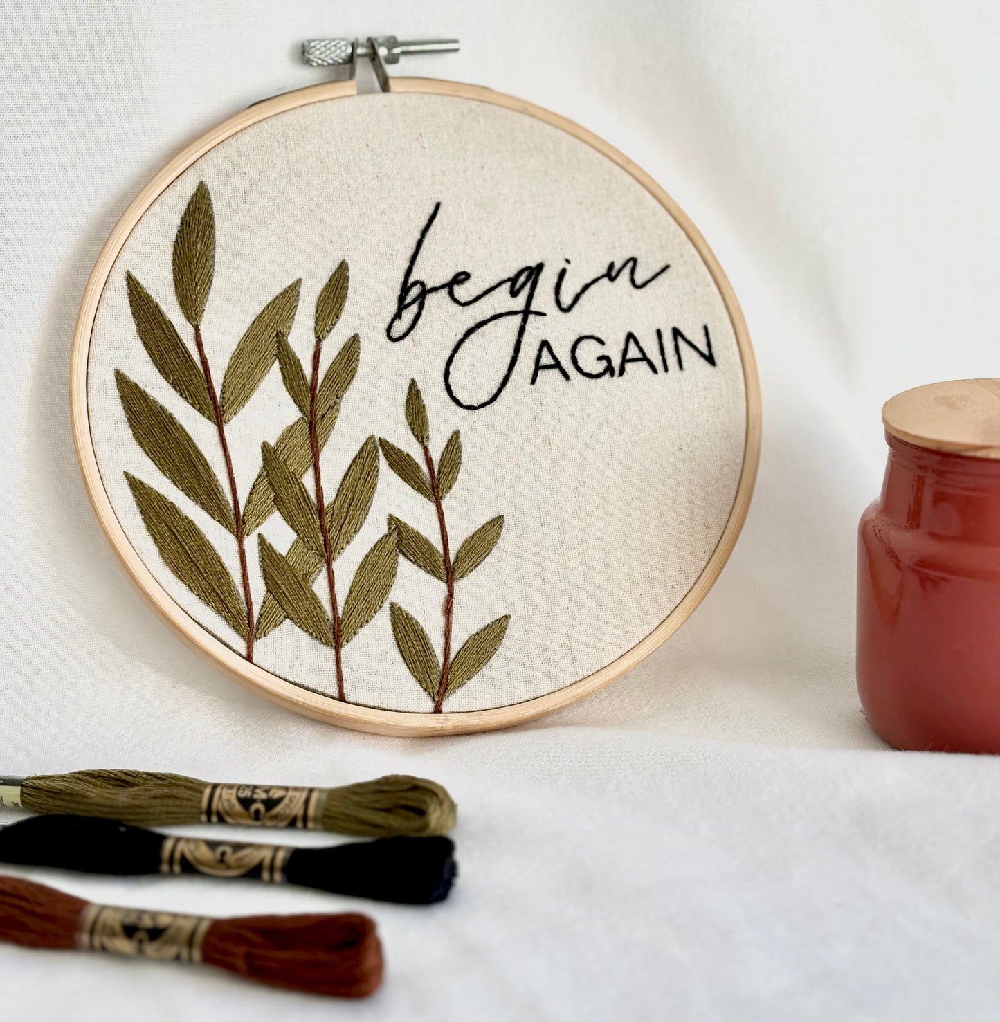 Bordado a mano decorativo incluido en kit de bordado para nivel principiante e intermedio, con hojas verdes bordadas y mensaje “begin again” en bastidor.