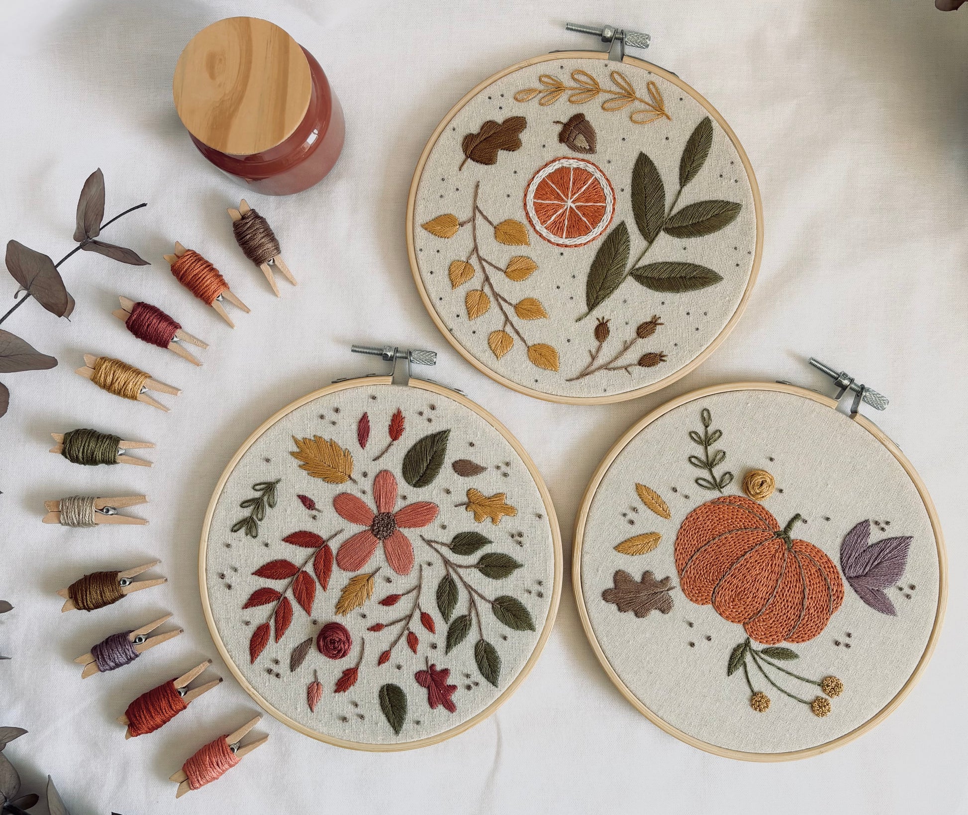 Bordados a mano terminados de la colección Otoño: diseño botánico con naranja seca, composición floral de otoño en rojos y ocres, y calabaza bordada en naranja con hojas moradas