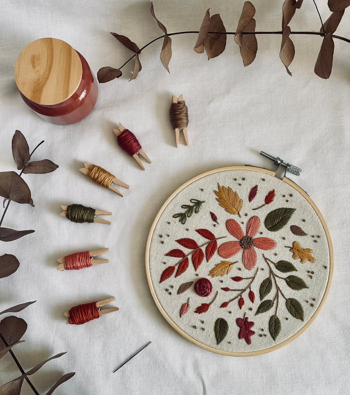 Bordado a mano terminado con diseño floral otoñal en rojos, rosas y verdes oscuros, con flores silvestres y hojas caídas, acompañado de hilos DMC en tonos cálidos