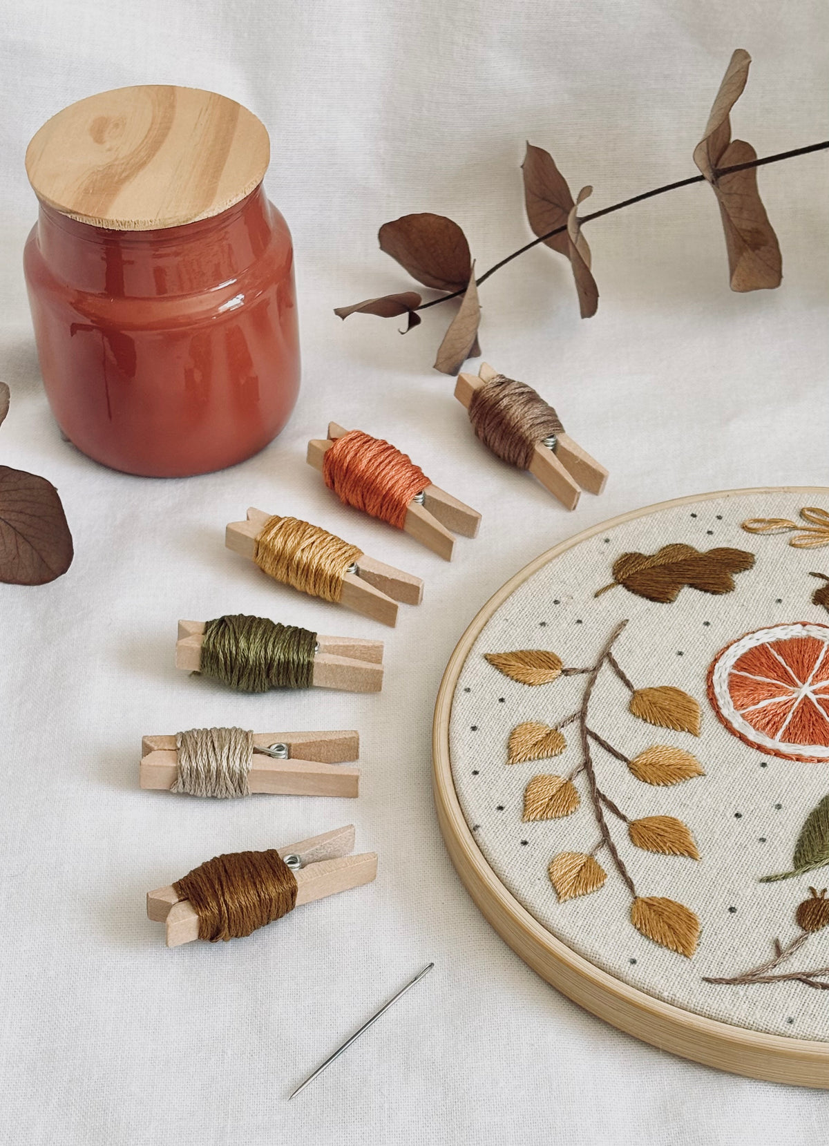 Detalle del bordado otoñal de naranja y hojas, junto a las madejas de hilo y una aguja de bordado